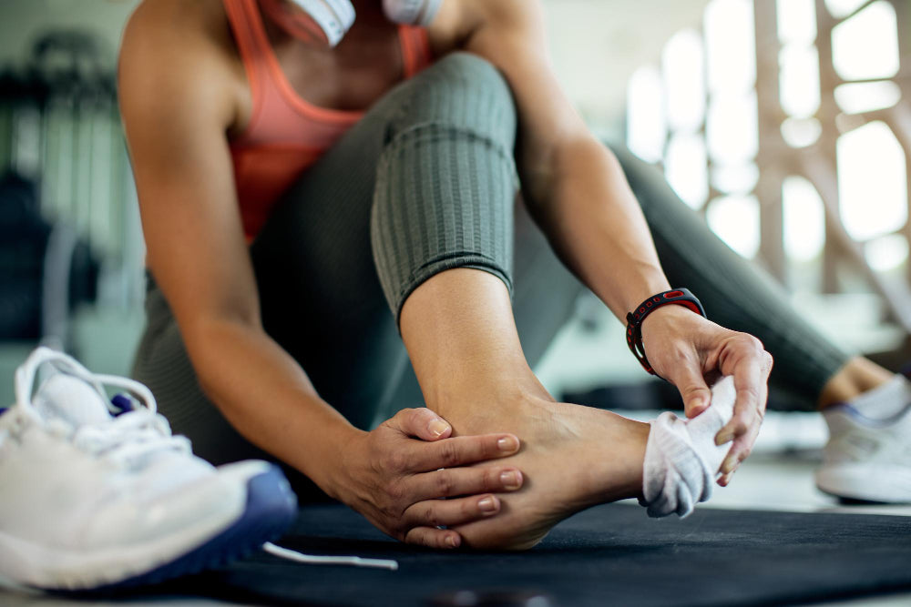 Woman in gym removing sock, dealing with recurring athlete's foot symptoms.