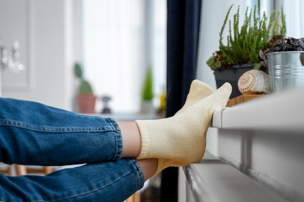Person wearing beige antifungal socks while resting their feet on a windowsill with plants and decorative items in the background.